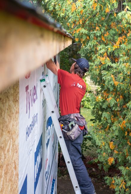 Construction worker on ladder preparing exterior for window installation
