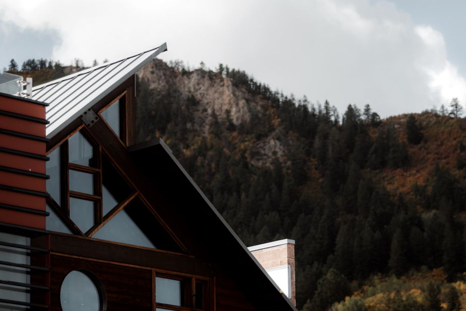 Modern house with red siding and metal roof against forested mountain backdrop