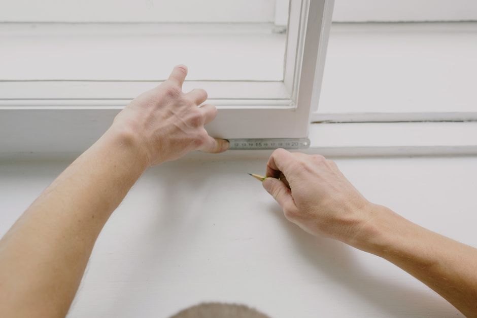 Measuring window frame with tape measure and pencil