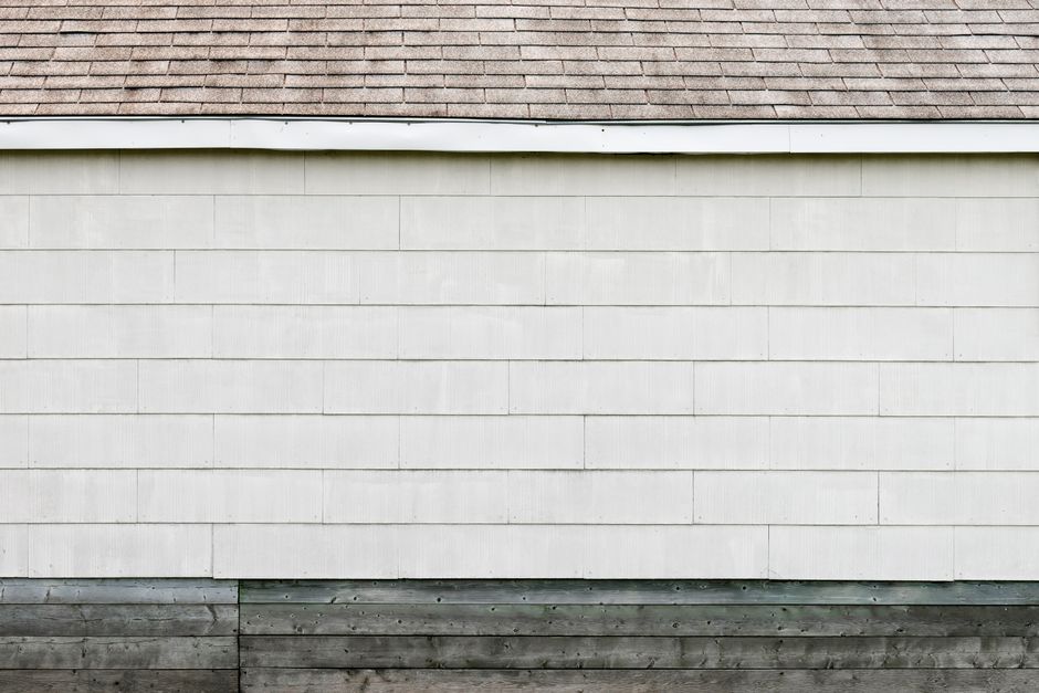 White horizontal lap siding on a house wall beneath an asphalt-shingle roof edge