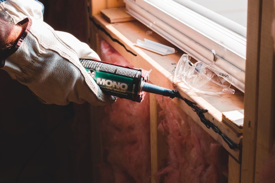 Close-up of a window sill and frame being sealed with caulk and weatherstripping
